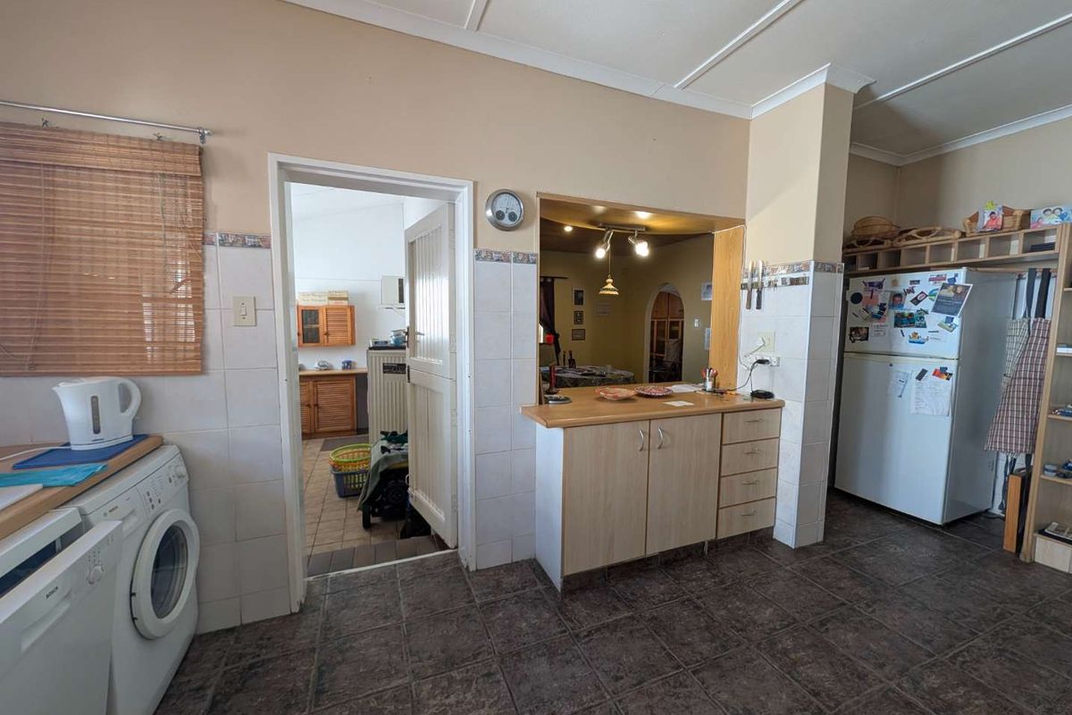 A functional kitchen area featuring tiled flooring, built-in cabinetry with laminate countertops, and a tiled splashback, with an adjacent doorway leading to a scullery.