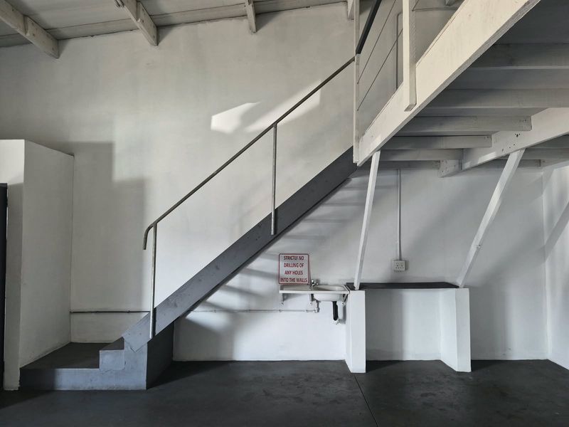 Industrial utility space featuring a mezzanine level, staircase, and a wall-mounted basin, offering versatile storage or workspace potential.