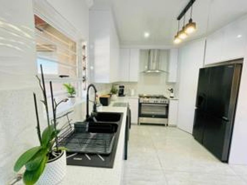 Modern kitchen featuring sleek white cabinetry, stone countertops, high-end stainless steel appliances, and contemporary pendant lighting.