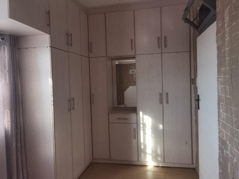 A bedroom featuring extensive built-in cabinetry with a central vanity mirror and light-toned laminate flooring.