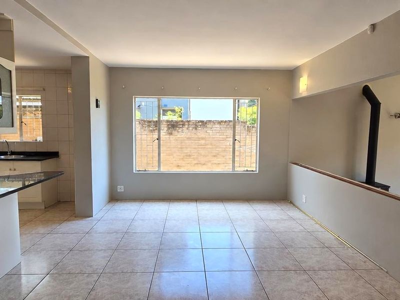 Spacious open-plan living and kitchen area featuring tiled flooring, granite countertops, and a built-in fireplace, offering a versatile layout for modern living.