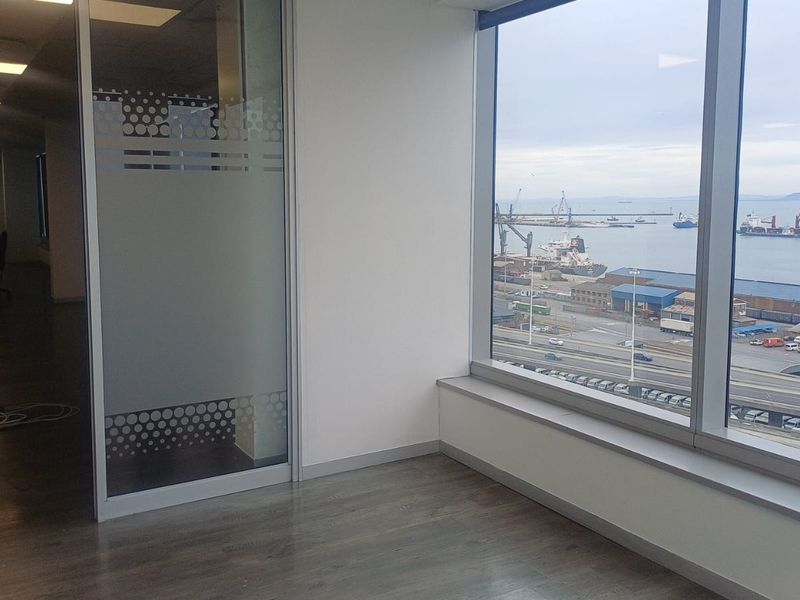 Modern office space featuring floor-to-ceiling windows with expansive harbour views, glass partition walls, and recessed ceiling lighting.