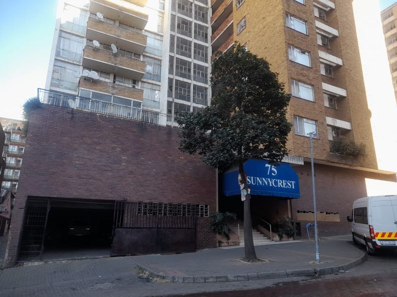 Street view of the Sunnycrest apartment building, featuring a brick facade, covered entrance, and secure parking access.