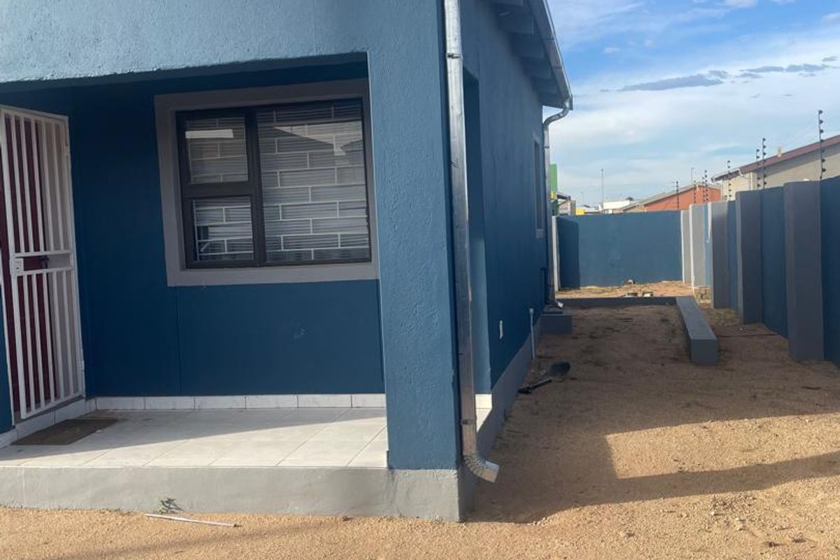 A side view of a blue-painted house featuring a small tiled patio, security gate, and a fenced perimeter wall.