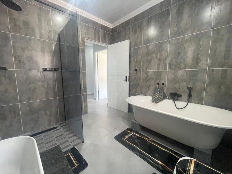 Modern bathroom featuring a freestanding bathtub, a spacious walk-in shower with glass screen, and contemporary large-format grey wall tiling.