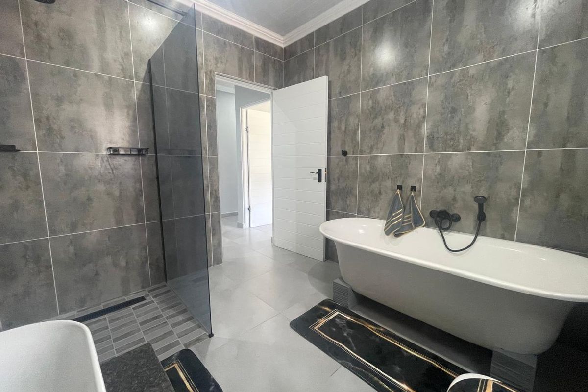 Modern bathroom featuring a freestanding bathtub, a spacious walk-in shower with glass screen, and contemporary large-format grey wall tiling.
