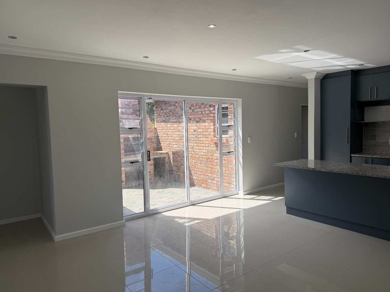 Spacious open-plan living area featuring polished tile floors, recessed lighting, and a modern kitchen island with granite countertops, leading to an outdoor patio.