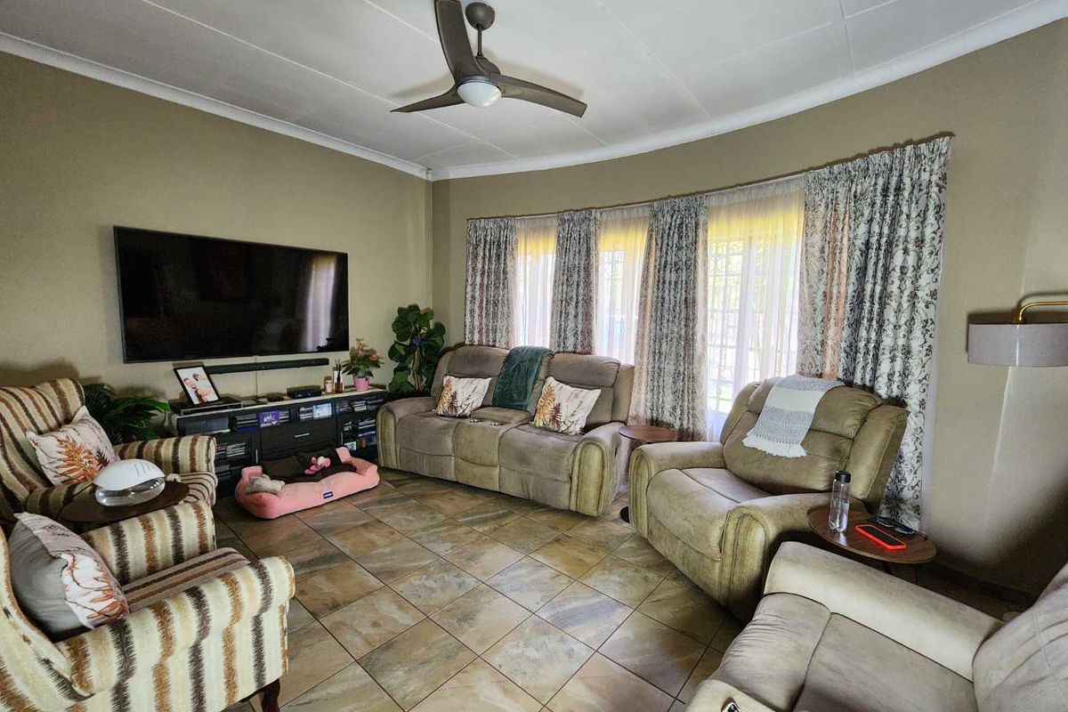 A comfortable living room featuring tiled flooring, a ceiling fan, and large windows with curtain treatments, providing a functional and inviting space.