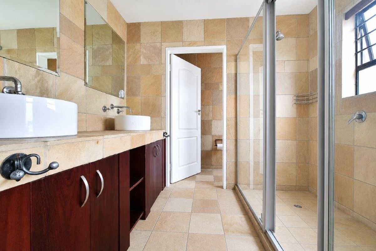 A spacious bathroom featuring a double vanity with vessel sinks, a walk-in shower with a glass enclosure, and neutral stone-look wall and floor tiling.
