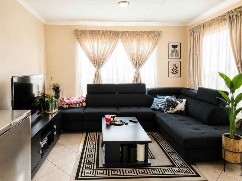 A comfortable living room featuring neutral wall tones, tiled flooring, and large windows with fitted curtain tracks.