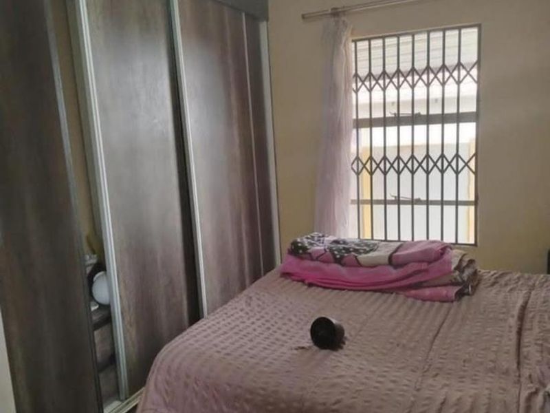 A bedroom featuring a large built-in sliding door wardrobe, tiled flooring, and a window fitted with a security gate.