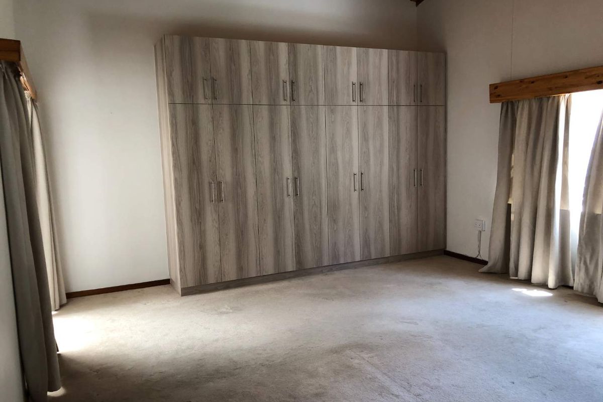 Spacious bedroom featuring extensive built-in cupboards, exposed timber rafters, and neutral carpeted flooring, offering a clean and functional living space.