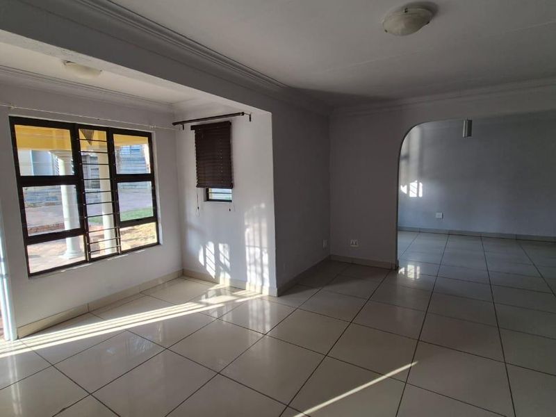 A spacious, empty living area featuring neutral tiled flooring, an arched entryway, and large windows with security bars, providing access to an outdoor patio.