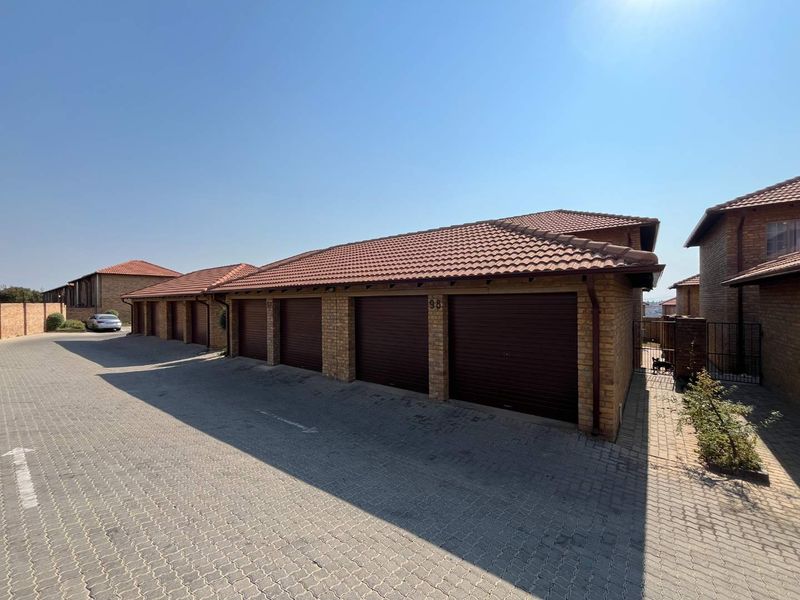 A row of brick-faced garages with tiled roofs and roll-up doors, situated along a paved driveway in a residential complex.