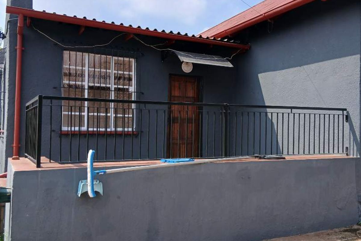 Rear exterior view of the house featuring a raised patio area with metal railings, security bars on windows, and a paved outdoor space.