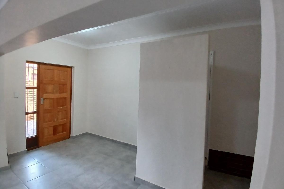 A clean, empty entrance area featuring neutral tiled flooring, a solid wooden panel door, and a central partition wall.