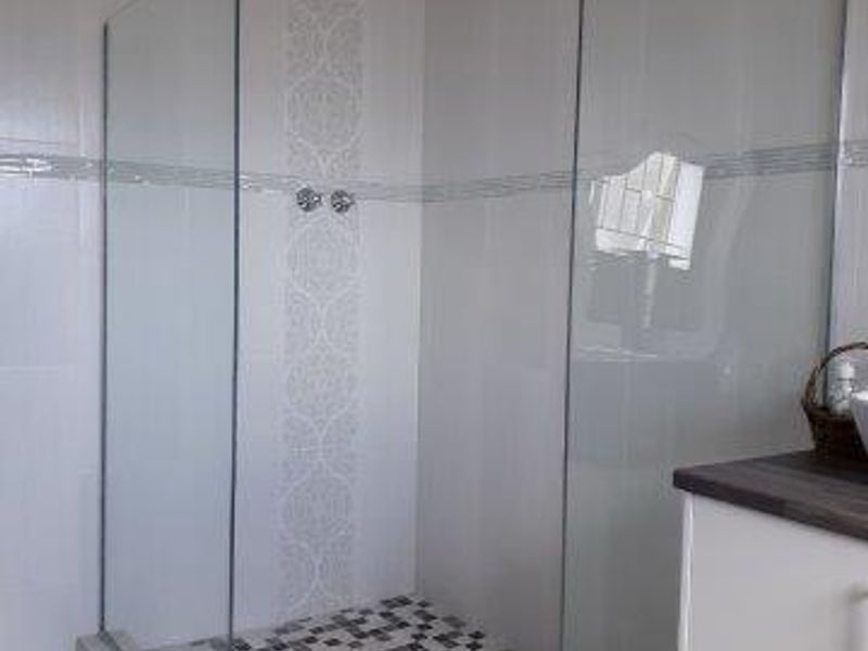 Modern bathroom featuring a spacious walk-in shower with a rainfall shower head, glass screens, and decorative tiled accents.
