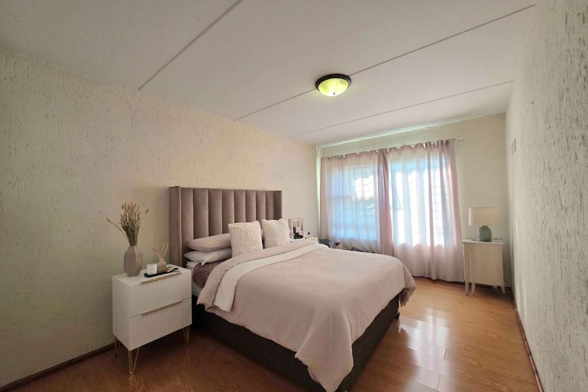 A well-lit bedroom featuring laminate flooring, textured walls, and a window fitted with security bars.