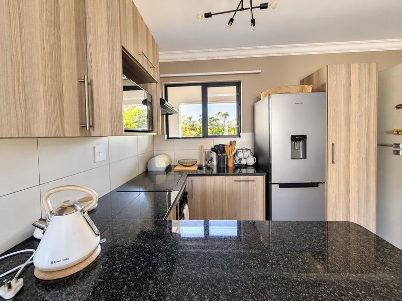 Modern kitchen featuring light wood-grain cabinetry, dark granite countertops, and integrated appliances, offering a clean and functional workspace.