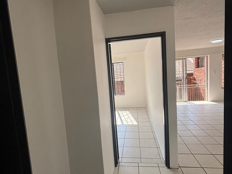 A bright, empty hallway with neutral ceramic floor tiles, leading into an open-plan living area with access to a balcony.