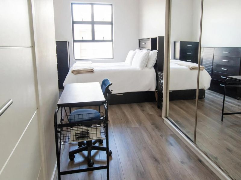 A well-maintained bedroom featuring modern laminate flooring, a large window for natural light, and a spacious built-in mirrored wardrobe.