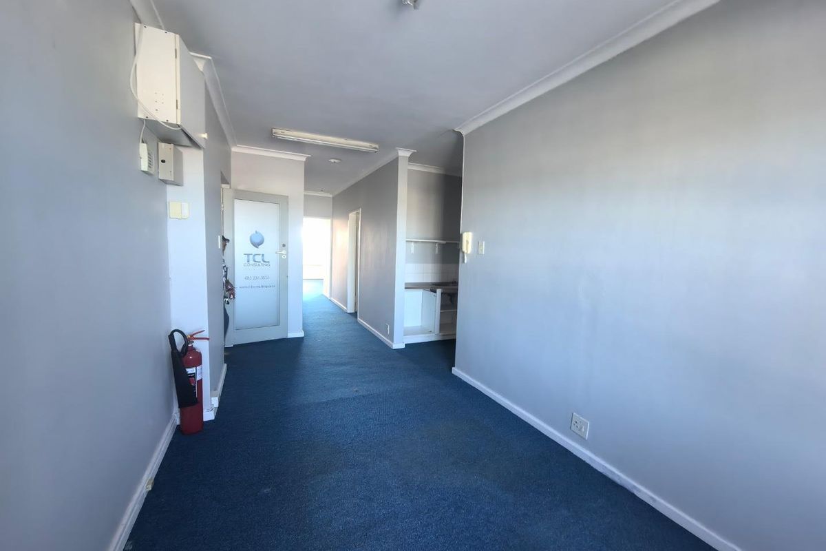 A functional office hallway featuring blue carpet flooring, fluorescent lighting, and a small kitchenette nook, providing access to multiple office spaces.