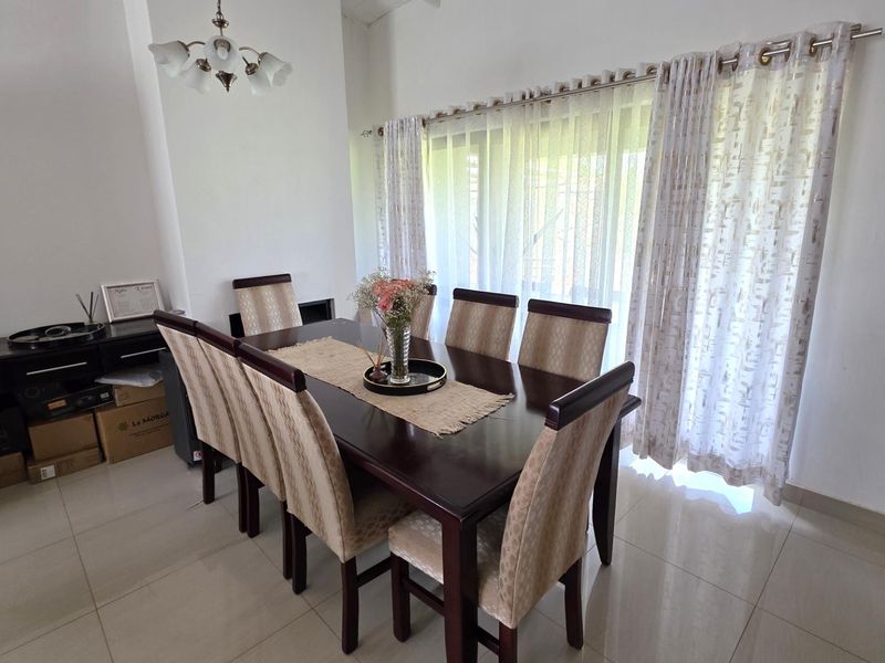 A bright dining room featuring neutral tiled flooring and large windows dressed with elegant curtains, providing a clean and functional space for family meals.