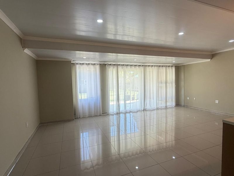 Spacious open-plan living area featuring polished tiled flooring, recessed downlighting, and large sliding glass doors providing natural light and garden access.