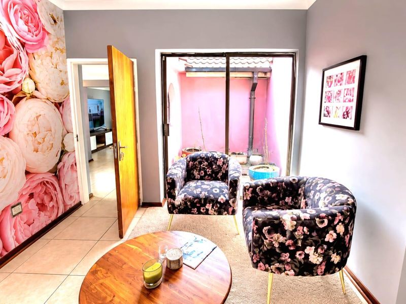 A living area featuring tiled flooring, a floral feature wall, and a sliding glass door providing access to an outdoor courtyard space.