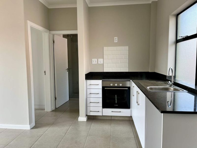 A clean, modern kitchen featuring white cabinetry, black granite countertops, a built-in oven, and a subway tile backsplash with neutral floor tiles.