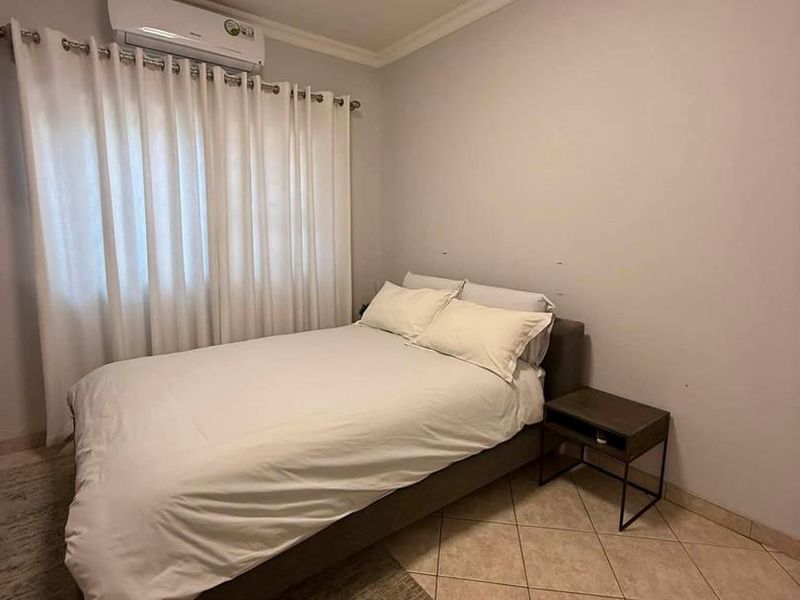 A functional bedroom featuring tiled flooring, a wall-mounted split-system air conditioner, and neutral wall finishes.