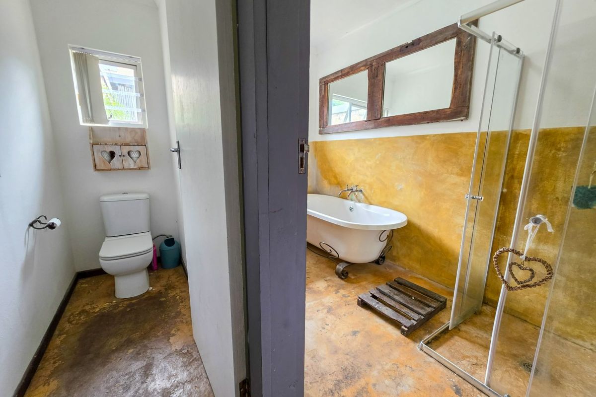 Bathroom featuring a freestanding bathtub, glass shower enclosure, and toilet, with a rustic yellow wall finish and worn flooring.
