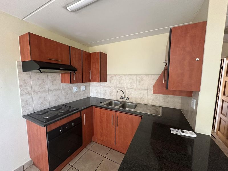 A functional kitchen featuring wood-look cabinetry, dark laminate countertops, a built-in oven with hob, and a stainless steel double sink with tiled splashbacks.