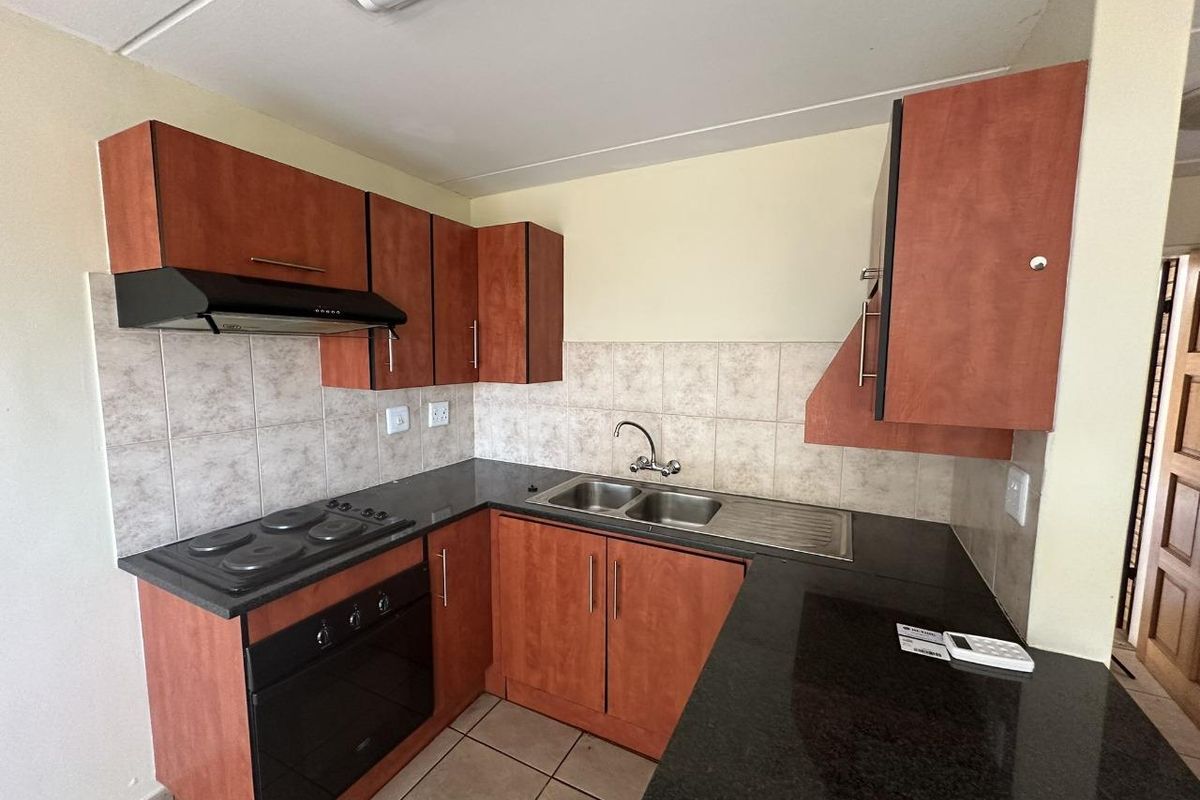A functional kitchen featuring wood-look cabinetry, dark laminate countertops, a built-in oven with hob, and a stainless steel double sink with tiled splashbacks.