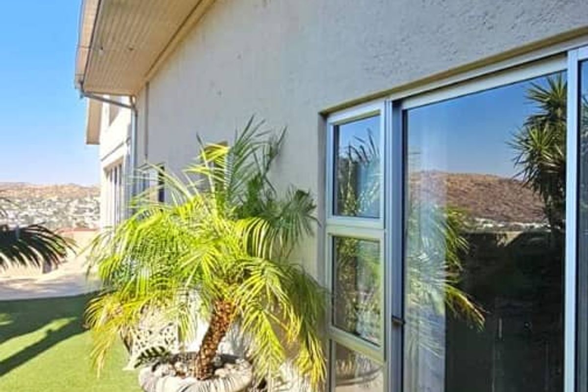 A view of the exterior rear facade featuring a covered patio area with sliding glass doors and artificial lawn.