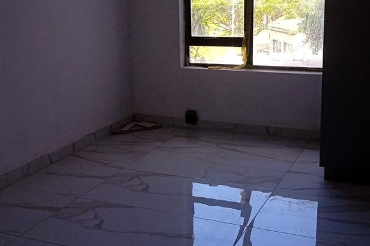 An empty bedroom featuring polished marble-look floor tiles, a large window with natural light, and a built-in cupboard.