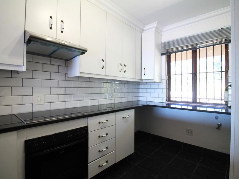 Modern kitchen featuring white cabinetry, black granite countertops, subway tile backsplash, built-in oven, and electric cooktop with an extractor fan.