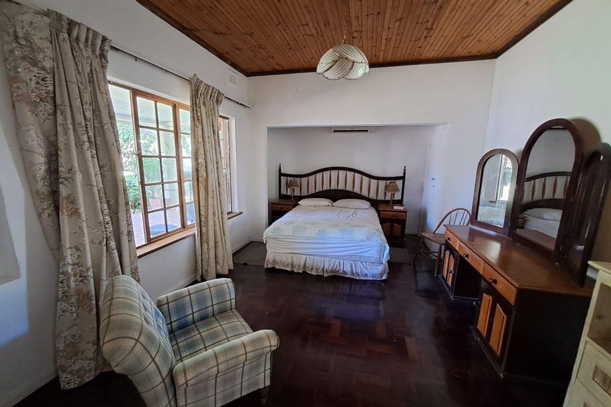 Spacious bedroom featuring dark timber parquet flooring, a traditional wood-paneled ceiling, and a wall-mounted air conditioning unit.