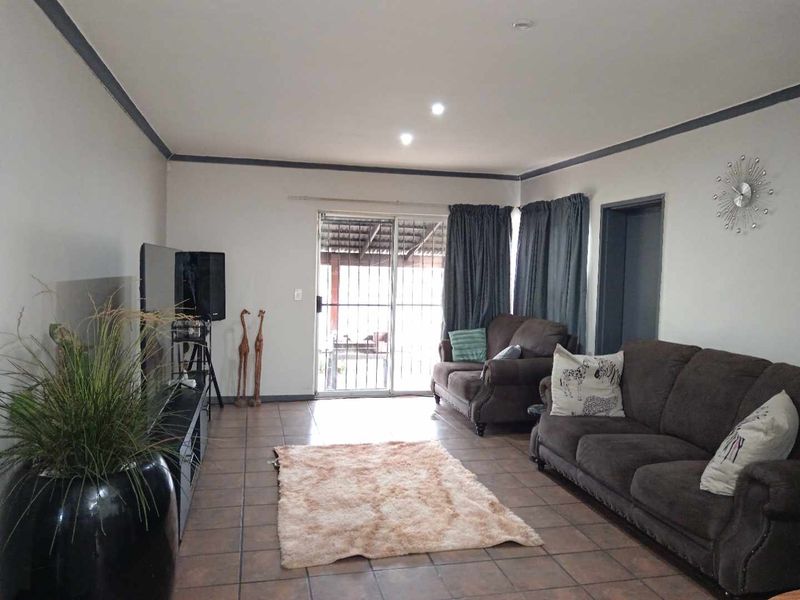 A spacious living room featuring tiled flooring, recessed lighting, and a sliding glass door providing access to the outdoor area.