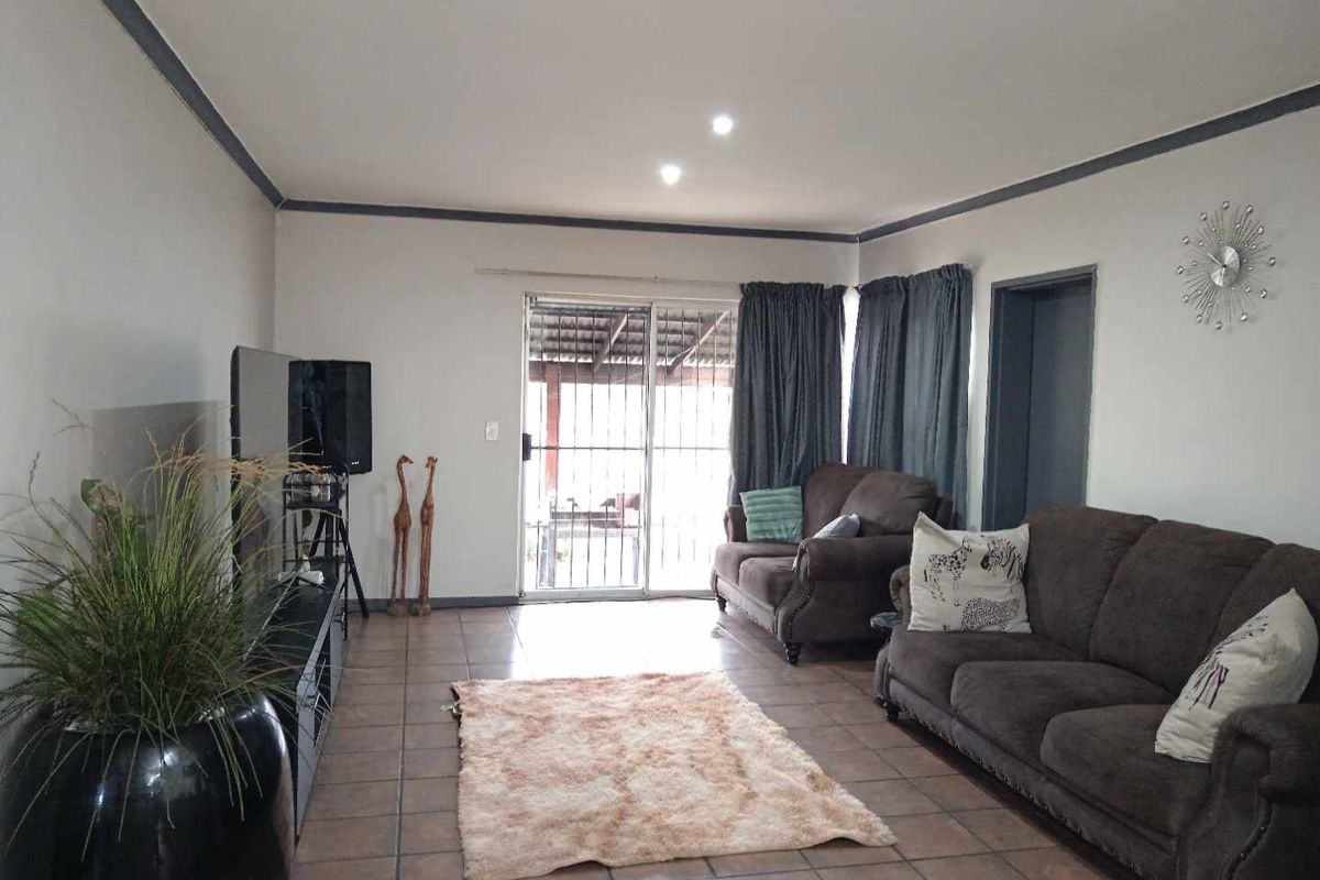 A spacious living room featuring tiled flooring, recessed lighting, and a sliding glass door providing access to the outdoor area.