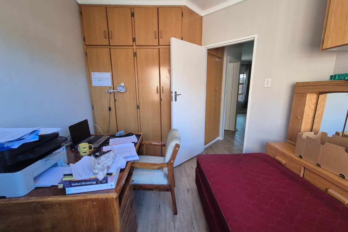 A functional bedroom featuring built-in wooden cupboards and laminate flooring, currently utilized as a study space.