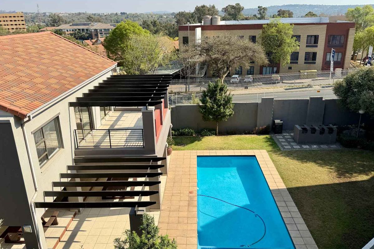 Aerial view of a residential property featuring a swimming pool, tiled patio area with pergola, and a landscaped garden with boundary wall.