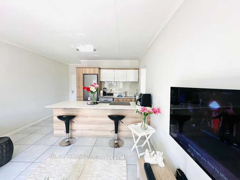 An open-plan living and kitchen area featuring a modern kitchen island, light wood-finish cabinetry, and neutral tiled flooring throughout.