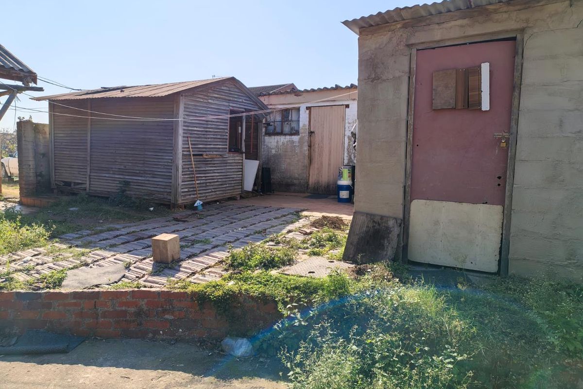 Rear yard area featuring a paved courtyard, brick retaining wall, and multiple outbuildings with weathered finishes and signs of significant wear.
