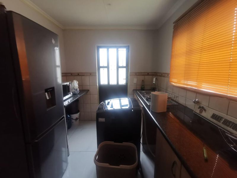 Functional scullery area featuring granite countertops, a stainless steel sink, tiled backsplash, and a secure exterior door with natural light.