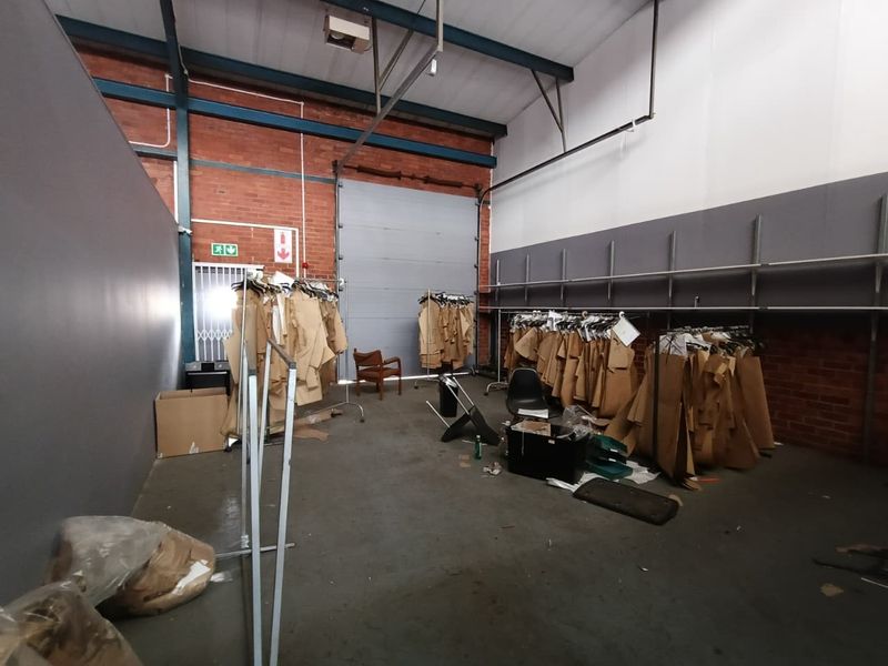 Industrial utility space featuring exposed brick walls, high steel roof trusses, concrete flooring, and a large roller shutter door for easy access.