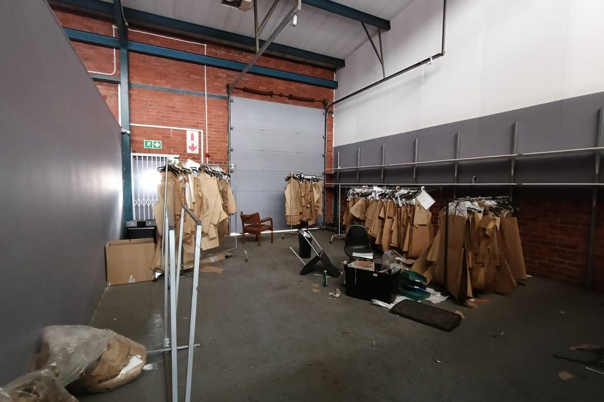 Industrial utility space featuring exposed brick walls, high steel roof trusses, concrete flooring, and a large roller shutter door for easy access.
