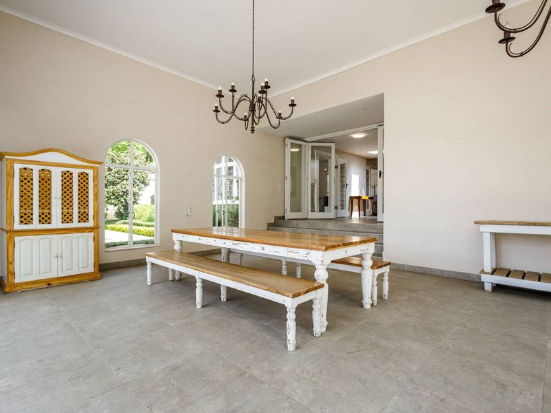Spacious dining area featuring large arched windows, neutral walls, tiled flooring, and elegant wrought iron chandeliers, with direct access to adjacent living spaces.