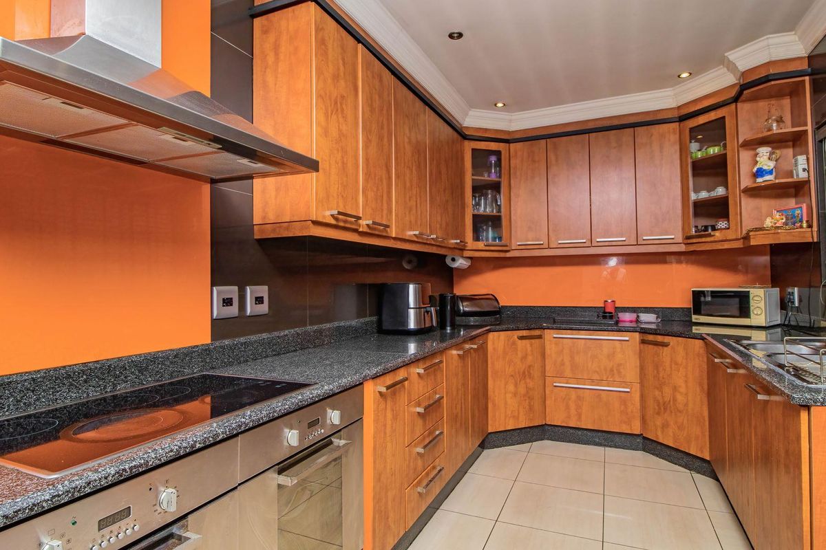 A functional kitchen featuring wooden cabinetry, granite countertops, a built-in oven, electric hob, and a stainless steel extractor fan.