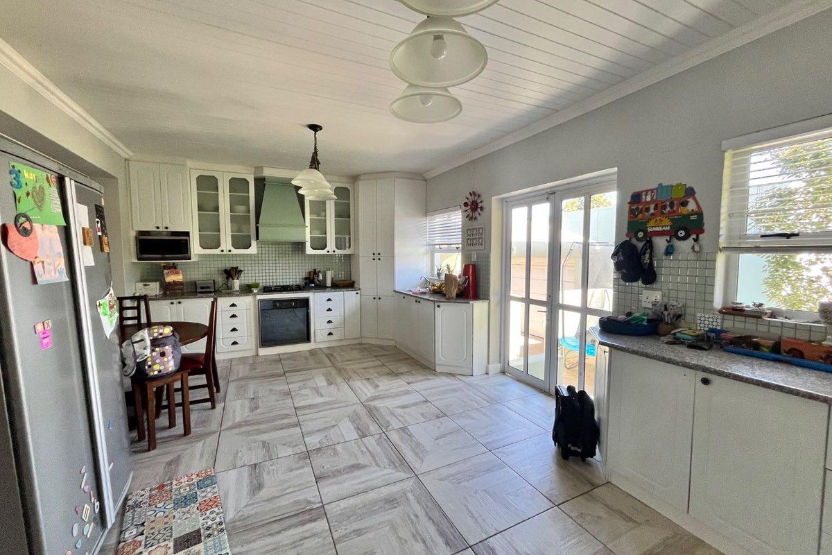 Spacious kitchen featuring white cabinetry, tiled backsplash, built-in appliances, and direct access to the outdoor area through glass doors.